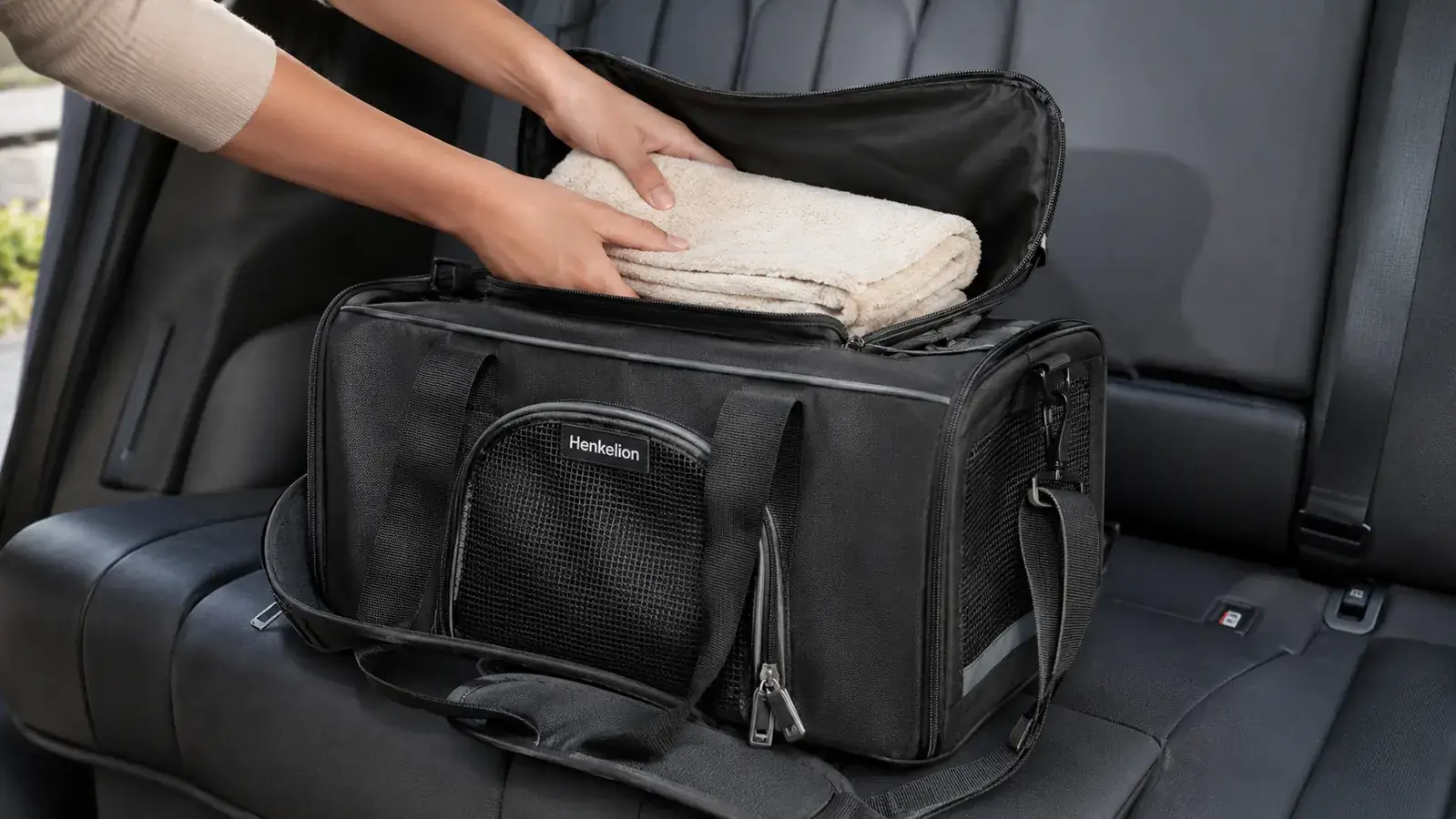 A person's hand tucking a folded towel into a soft-sided carrier that rests on a car back seat